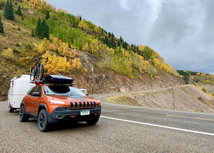 orange jeep towing white camper around curvy mountain road fall colors colorado