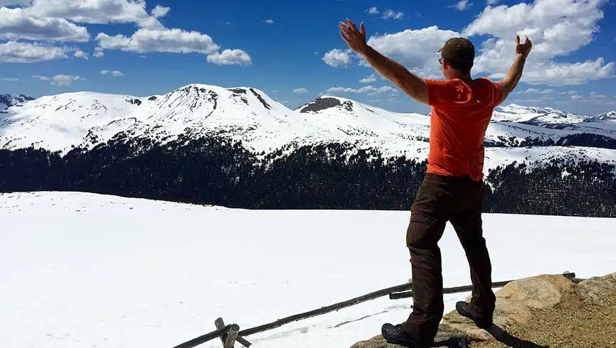 Man on snowy colorado mountain ledge with arms stretched out