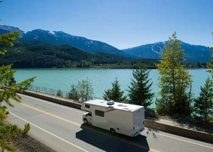 rv drives on road by lake in canada