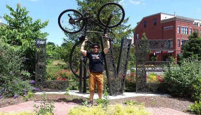 man lifting bike above head in front of a bicycle themed love works sign in Virginia
