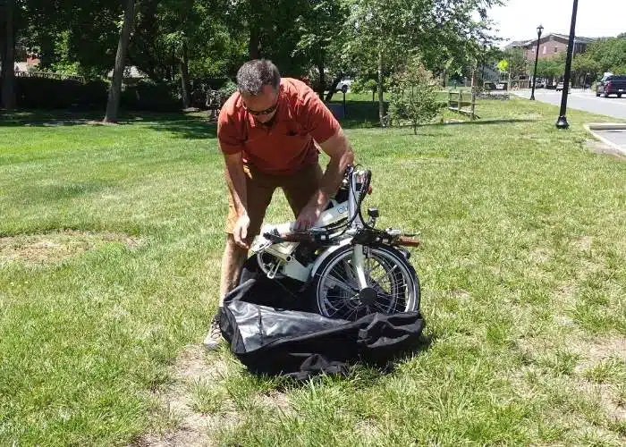 man pulling folded up bike out of a bag in grassy area