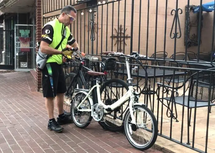 man locking bike to metal fence on brick sidewalk
