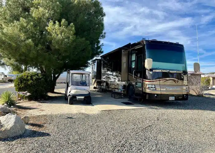class a rv and golf cart at jojoba hills resort with a large tree