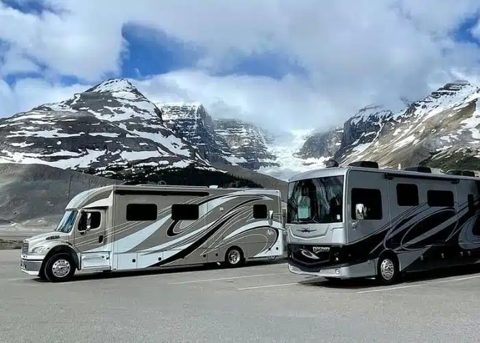 Photo Credit_ Tati McAlister Class C Motorhome and Class A motorhome parked in lot with snow capped mountains clouds and blue sky