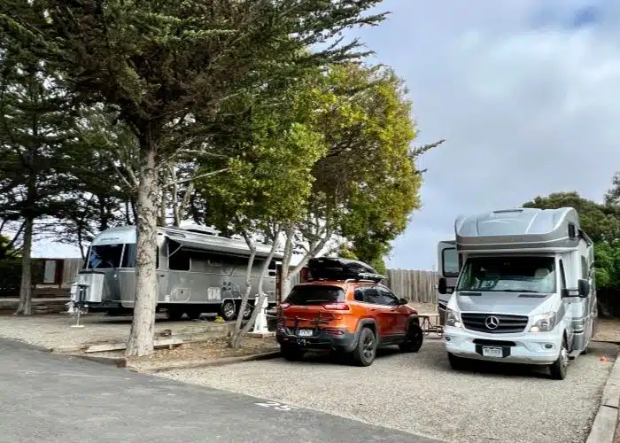 airstream and class c motorhome and jeep parked in campsites ay marina dunes rv resort monterey with trees and cloudy blue sky