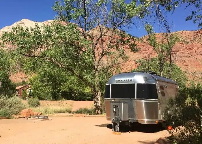 airstream trailer parked in scenic campsite at zion trees and red rocks behind