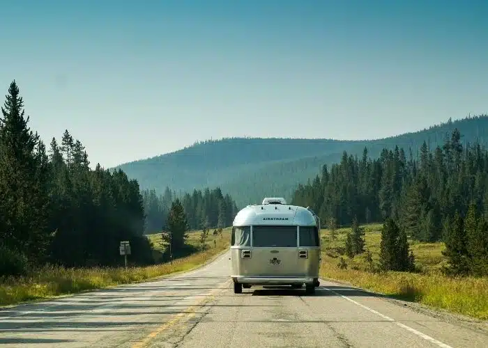 back of airstream trailer being towed along quiet scenic road trees and mountains