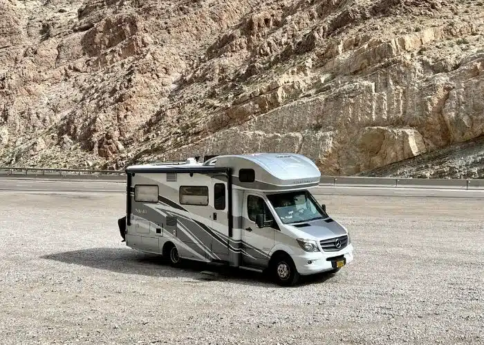class c motorhome parked on side of road with big rock wall behind