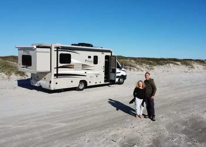 couple stands by rv motorhome parked on beach