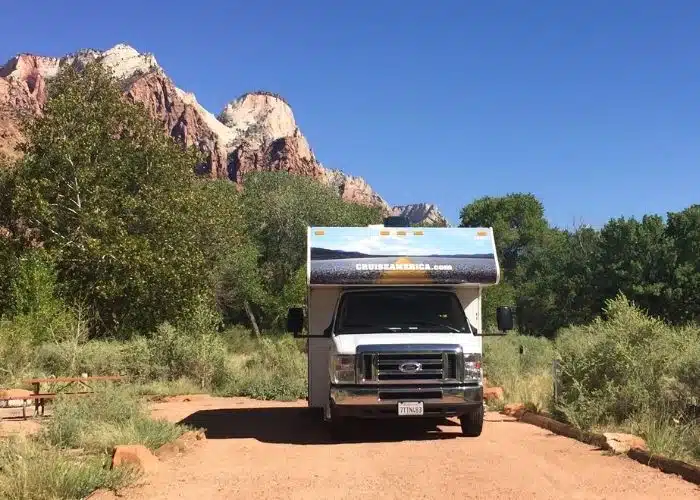 cruise america class c rental rv parked in campsite at zion np with trees blue sky red rocks