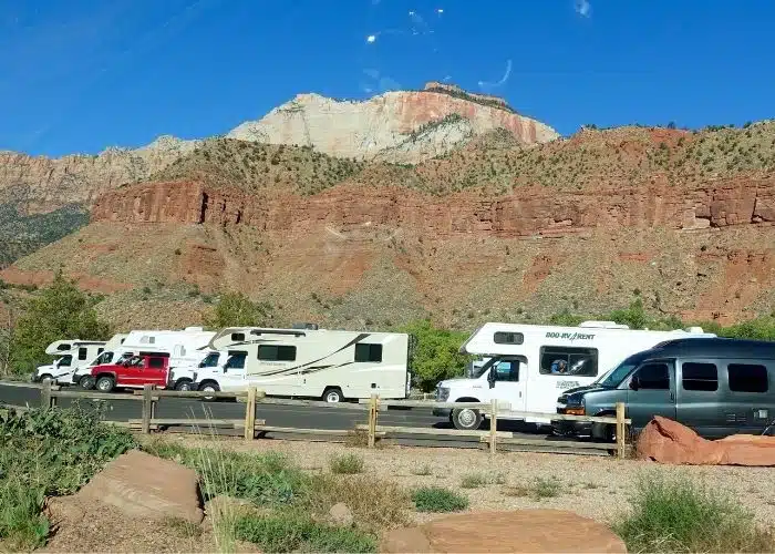 many small motorhomes in zion np parking lot red rocks blue sky views