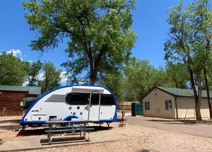 small travel trailer parked in campsite picnic table bathhouse trees blue sky