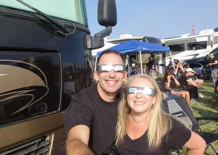 couple wearing eclipse glasses smiling in front of their rv