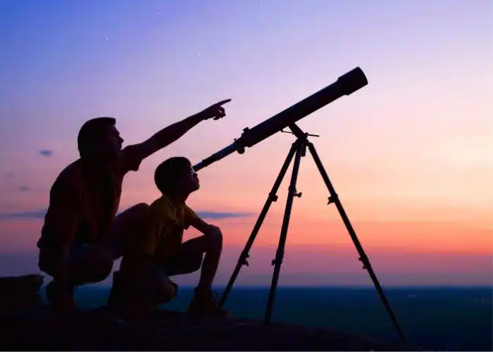 man and child look through telescope pink purple night sky