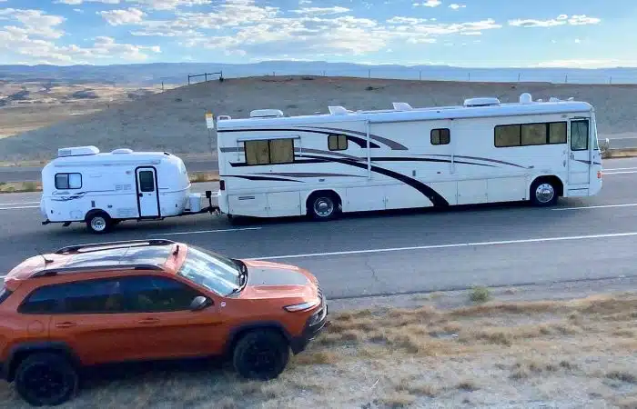 40' white motorhome towing small casita camper with orange jeep in foreground