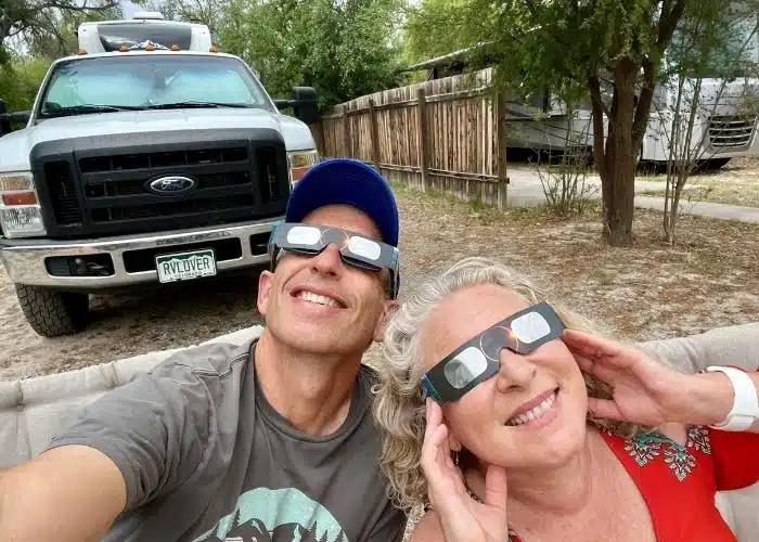 marc and julie smiling wearing eclipse glasses looking up at sky with truck and rv behind