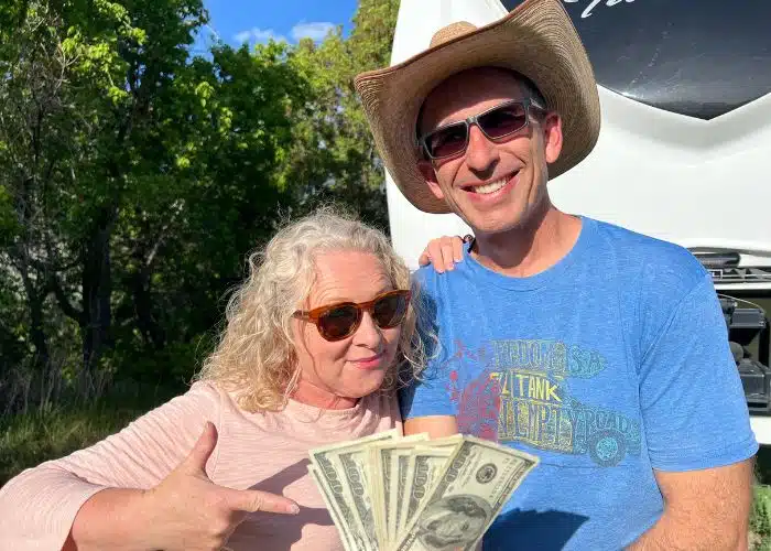 marc and julie stand in front of rv pointing at a wad of cash