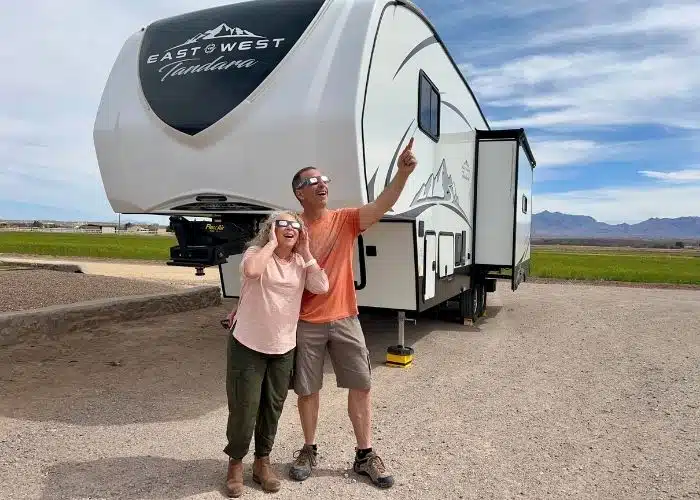 marc and julie wearing eclipse glasses pointing at sky by fifth wheel