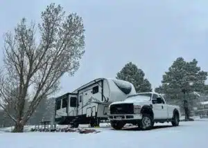 white truck and fifth wheel parked in campsite surrounded by snow