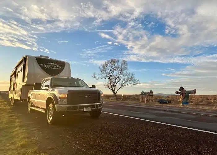 white truck and rv parked by giant movie set display at sunset tree and blue sky clouds